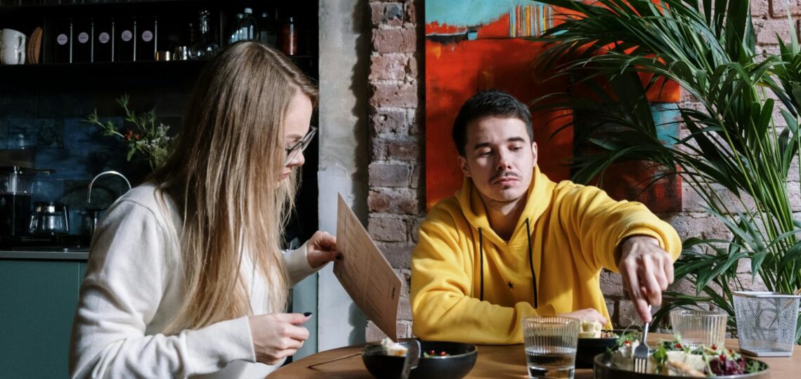 casal em um restaurante se alimentando. A mulher está com um cardápio em sua mão