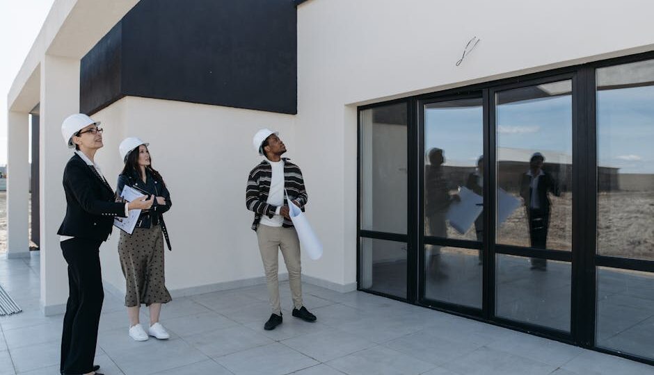 Architects in hard hats discuss the structure of a new building with large glass doors, suggesting a modern architectural design.